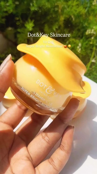 A close-up, high-contrast shot of a Vitamin C moisturizer jar being held against a natural green background to emphasize product freshness.